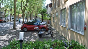 A street with parked cars and a scooter, trees lining the sidewalk, and a building with large windows. - Hotel Cristoforo Colombo (Cesenatico)