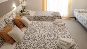 A hotel room with two beds, striped walls, a mirror, and a window with curtains. - Hotel Cristoforo Colombo (Cesenatico)