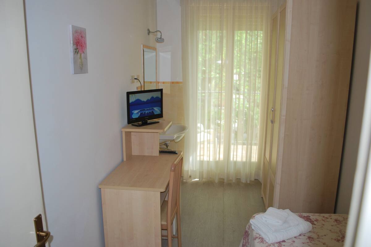 Ein Hotelzimmer mit Holztisch, Fernseher, einem Bett mit floralem Überwurf und einem Badezimmer mit Dusche und Spiegel.