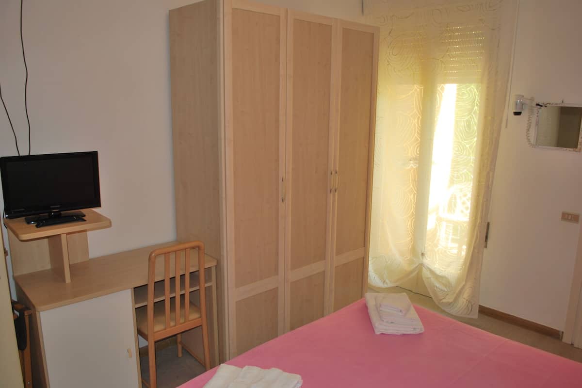 Ein Schlafzimmer mit einem Bett, einem Schreibtisch mit Computer, einem Kleiderschrank und einem Fenster mit Vorhängen.