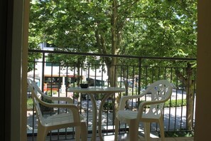 A balcony with two white plastic chairs and a small round table, overlooking a street with trees and buildings. - Hotel Cristoforo Colombo (Cesenatico)