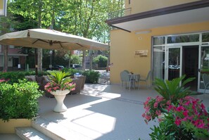 An outdoor patio area with a white umbrella, seating, and potted plants. - Hotel Cristoforo Colombo (Cesenatico)