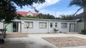 A building with a gravel driveway, a brick pathway, and a small garden area. - The Monument Guesthouse (Gqeberha)