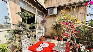 A red table and chairs set outdoors with potted plants and flowers around. - Aira Xing (New Delhi)