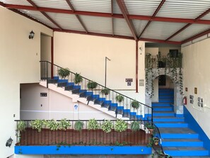 Una escalera con escalones azules que conduce a una plataforma, rodeada de plantas en macetas y una barandilla de metal.