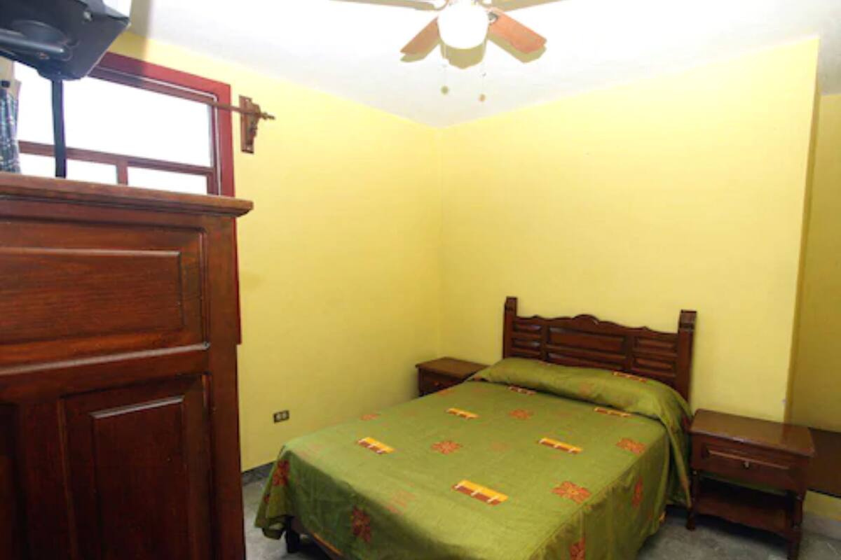 A bedroom with a wooden bed, a nightstand, a dresser, and a ceiling fan.