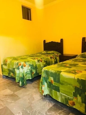 Una habitació amb dos llits, cadascun amb un estovat floral verd, una finestra petita i un terra d'rajola.