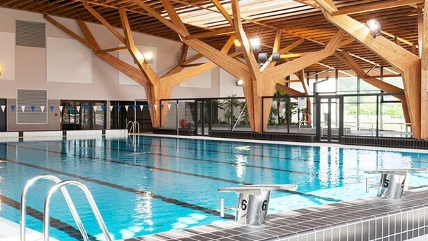 Una piscina al coperto con travi in legno, acqua cristallina e corsie numerate.