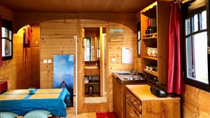 Interno di una baita in legno con zona pranzo, cucina e vista sull'esterno.