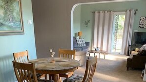 A dining area with a round table and four chairs, a sofa, and a TV in a living room with a carpeted floor.