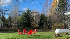 A grassy backyard with a picnic table and red chairs, surrounded by trees and a white structure.