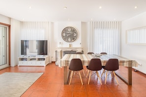A modern dining area with a large table, four chairs, a clock, and a television.