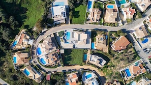An aerial view of a residential area with multiple houses, each featuring a swimming pool and a curved driveway.