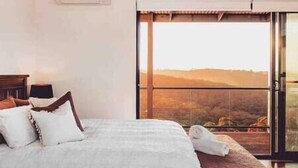 A bedroom with a large bed, a nightstand, and a view of a landscape through a sliding glass door.