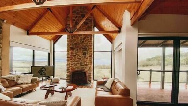 A spacious living room with a stone fireplace, leather sofas, and large windows offering a view of the landscape.