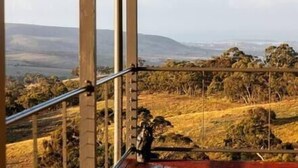 A view from a balcony with a metal railing, overlooking a hilly landscape with sparse vegetation and distant hills.