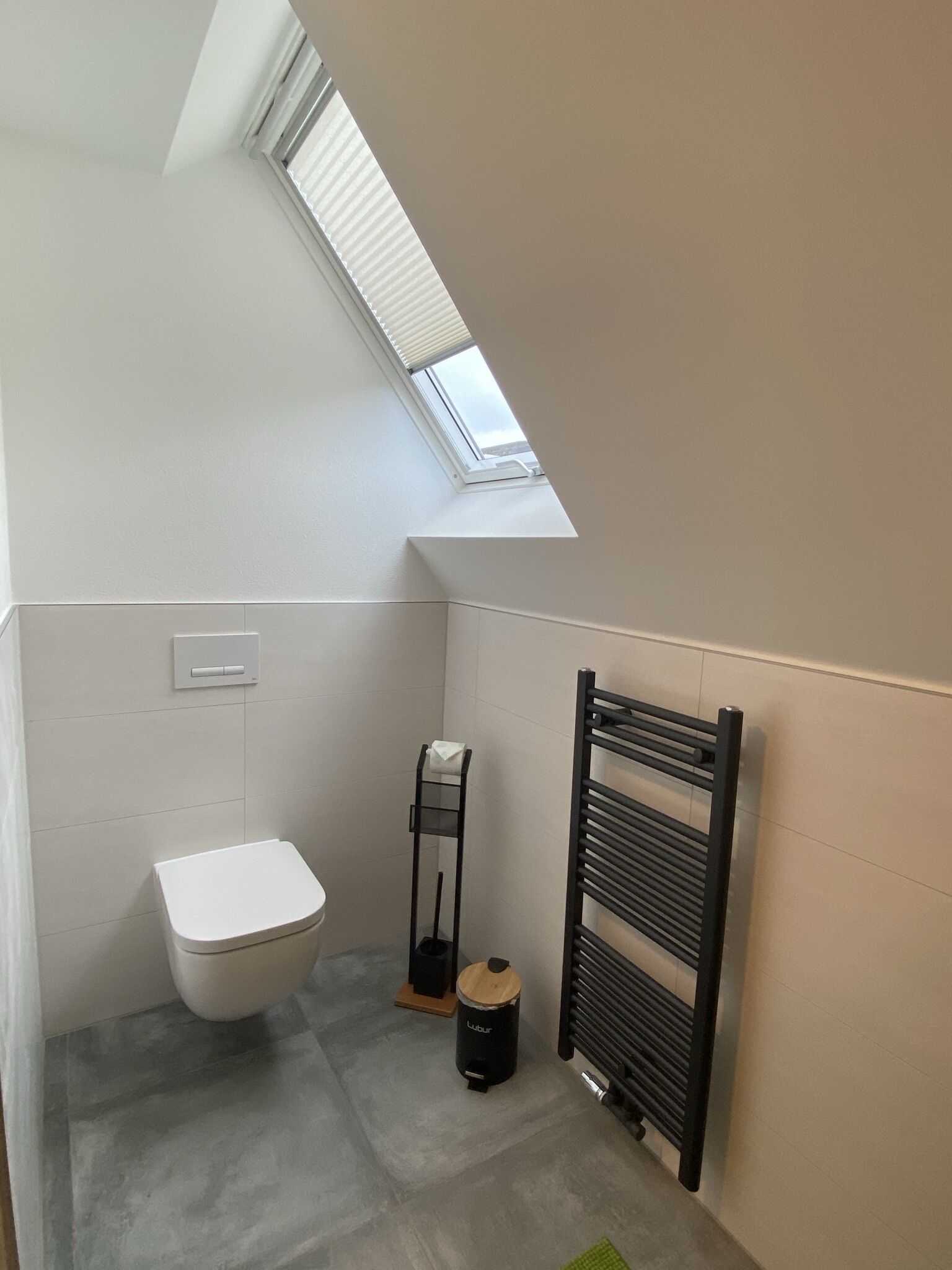Ein kleines, modernes Badezimmer mit Oberlicht, Toilette, Handtuchhalter und Heizkörper.