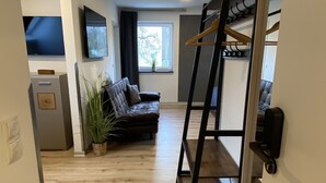 A modern living room with a sofa, a TV, a window, and a coat rack. - my inn (Chemnitz)