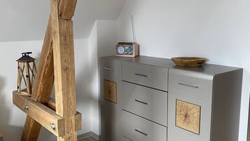 Una habitación con estructura de vigas de madera, un mueble gris con cajones, una radio y una pequeña mesa con un cuenco.