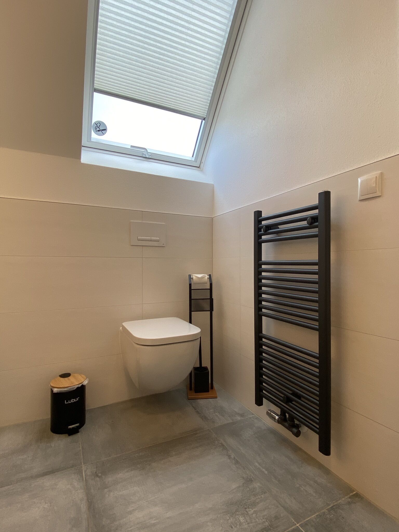 A bathroom with a skylight, a toilet, a towel rack, and a trash bin.