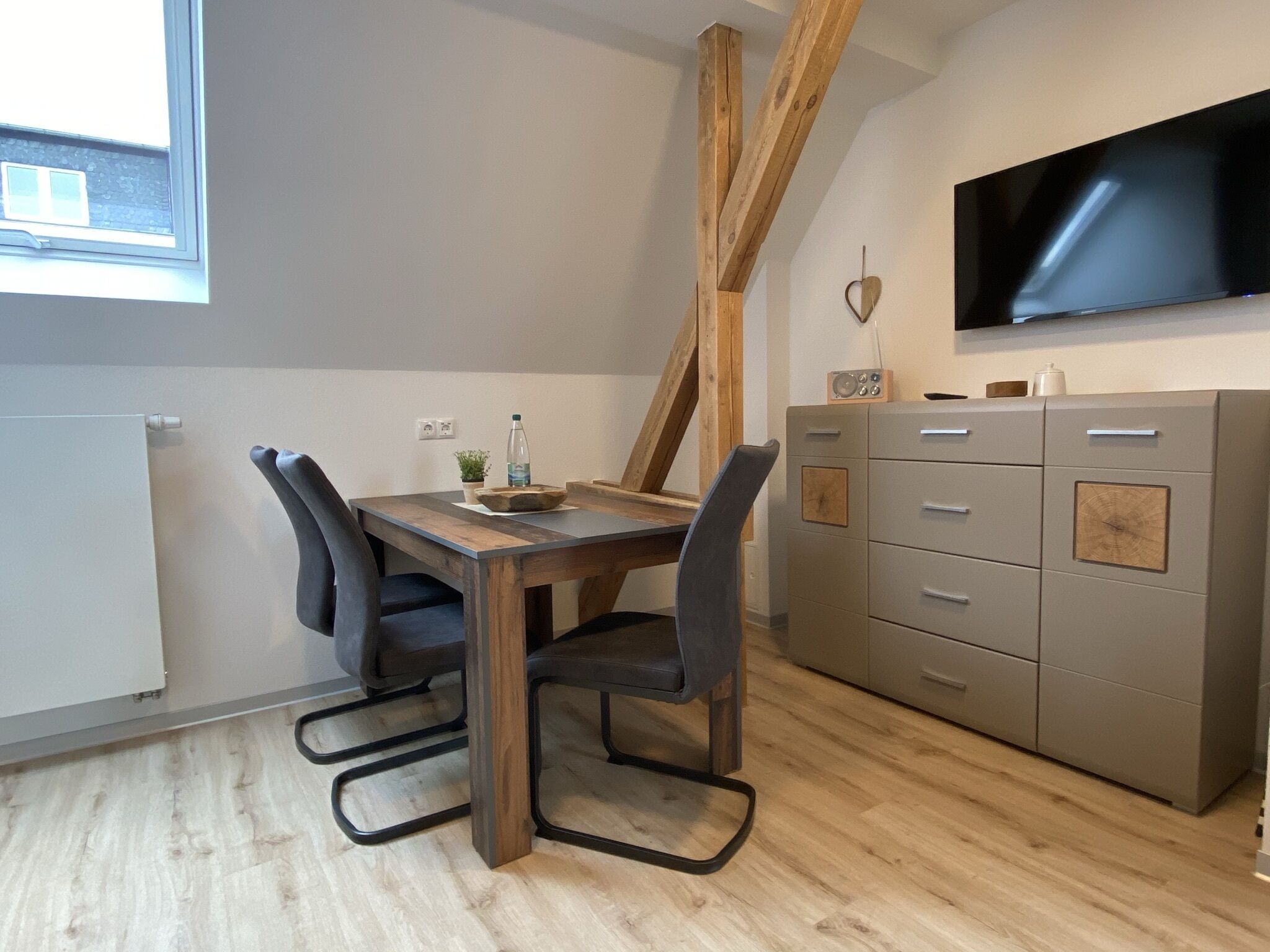 Un comedor moderno con una mesa y sillas de madera, un televisor montado en la pared y un mueble con cajones.