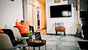 A modern living room with a sofa, a coffee table with a sign, a TV mounted on the wall, and a staircase. - my inn (Chemnitz)