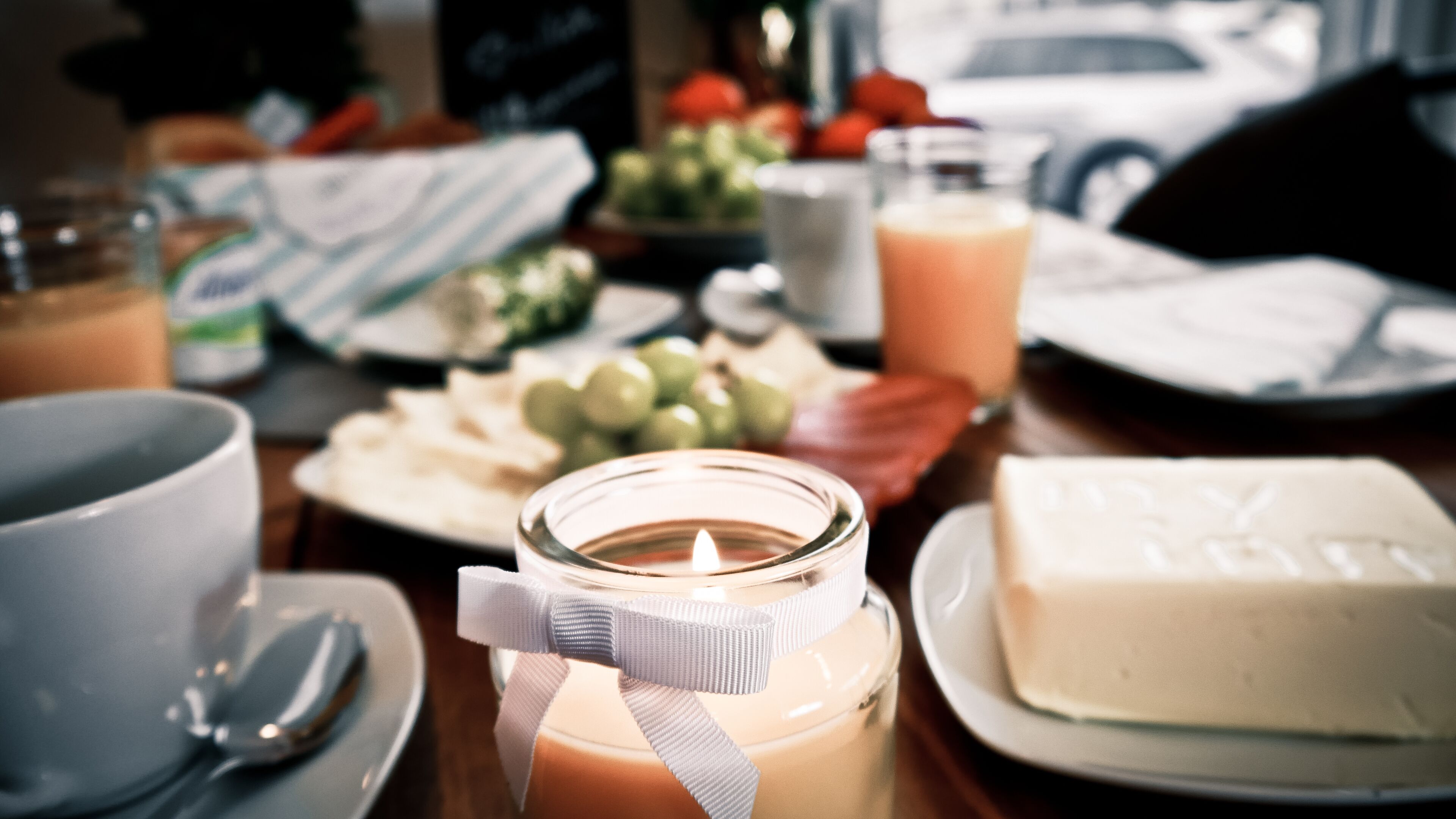Una mesa de desayuno con una vela, queso, uvas y un vaso de jugo de naranja.