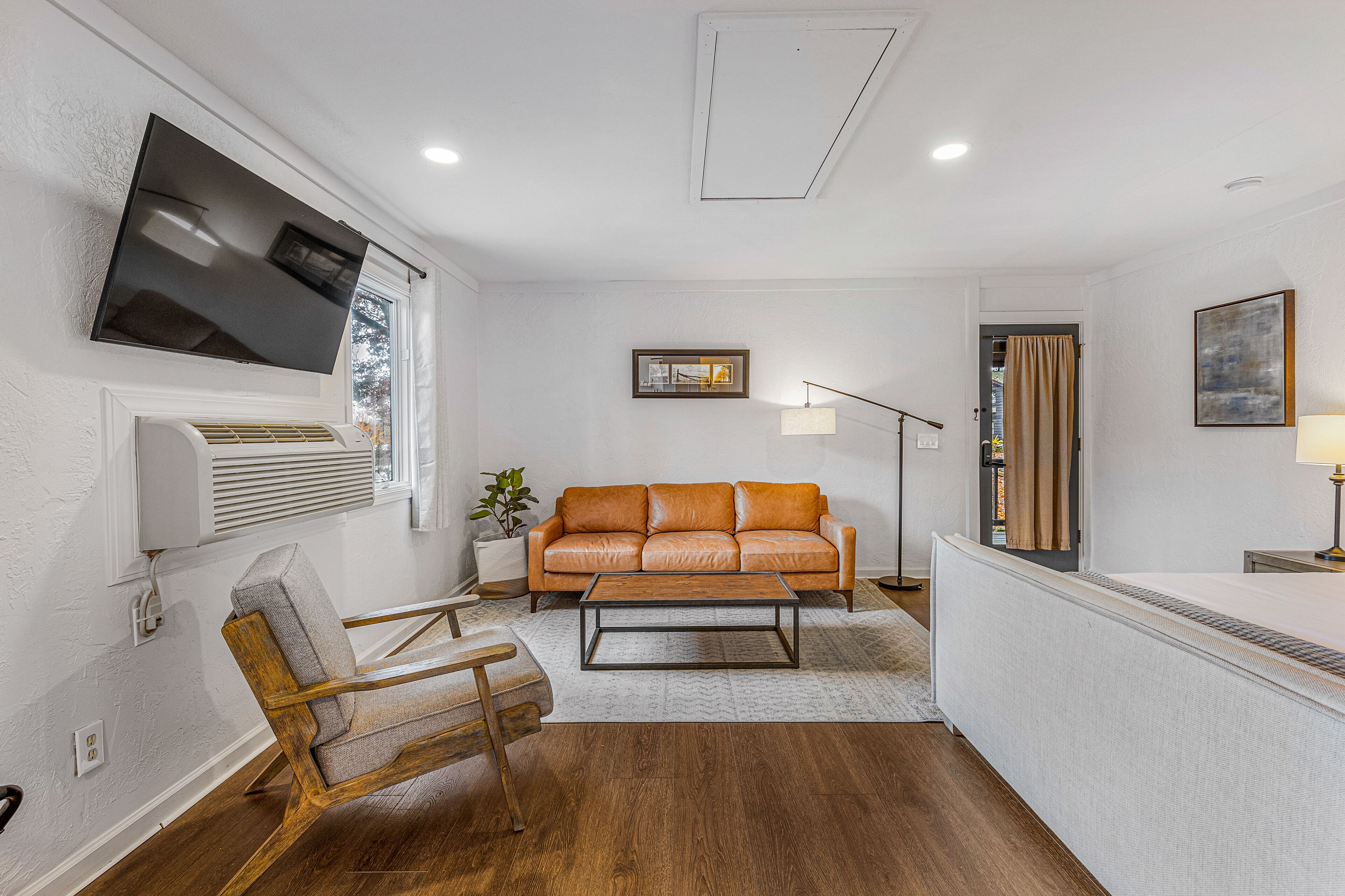 A modern living room with a leather sofa, a wooden chair, a flat-screen TV, and a floor lamp.