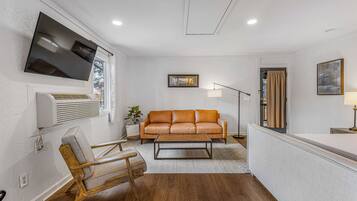 A modern living room with a leather sofa, a wooden chair, a flat-screen TV, and a floor lamp.