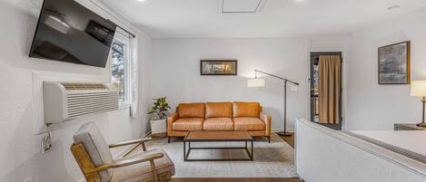Una sala de estar moderna con un sofá de cuero, una silla de madera, un televisor de pantalla plana y una lámpara de pie.