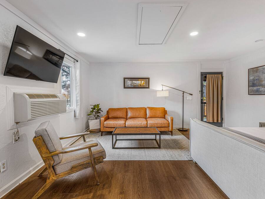 A modern living room with a leather sofa, a wooden chair, a flat-screen TV, and a floor lamp.