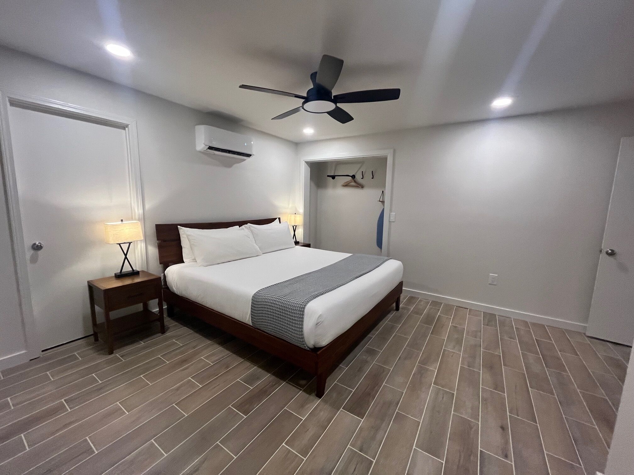 Ein Schlafzimmer mit Bett, Nachttisch, Deckenventilator, Klimaanlage und einer Tür.