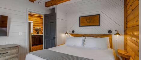 Un dormitorio con techo de madera, una cama con ropa de cama blanca, una mesita de noche y un cuadro colgado en la pared.