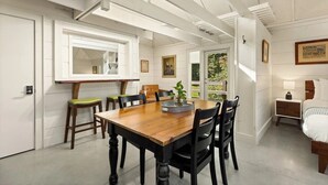 A dining area with a wooden table and chairs, a kitchen with white cabinets, and a bedroom with a bed and nightstand. - The Wells Hotel Cashiers (Cashiers)