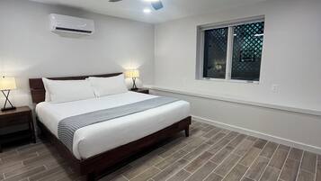 Un dormitorio con cama, mesitas de noche, ventilador de techo, aire acondicionado y ventana con vistas.
