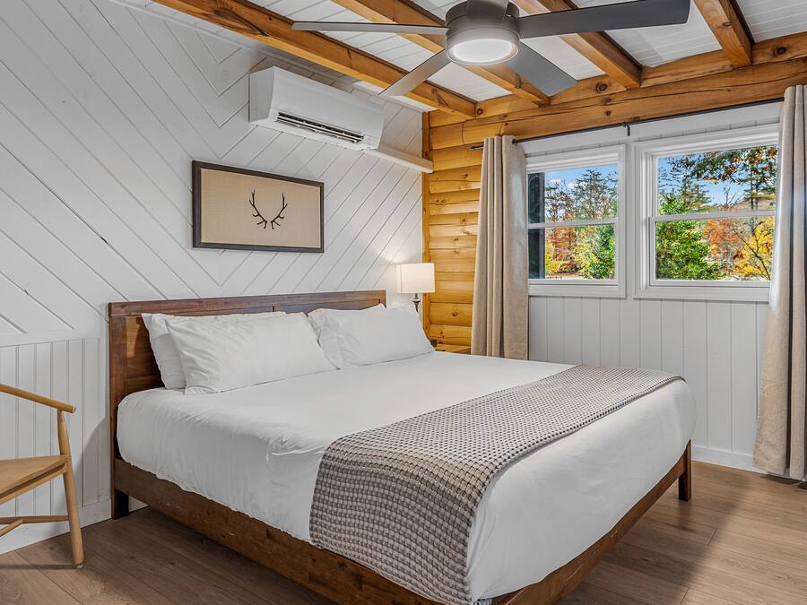 A bedroom with a wooden bed, white walls, a ceiling fan, and a window with curtains.