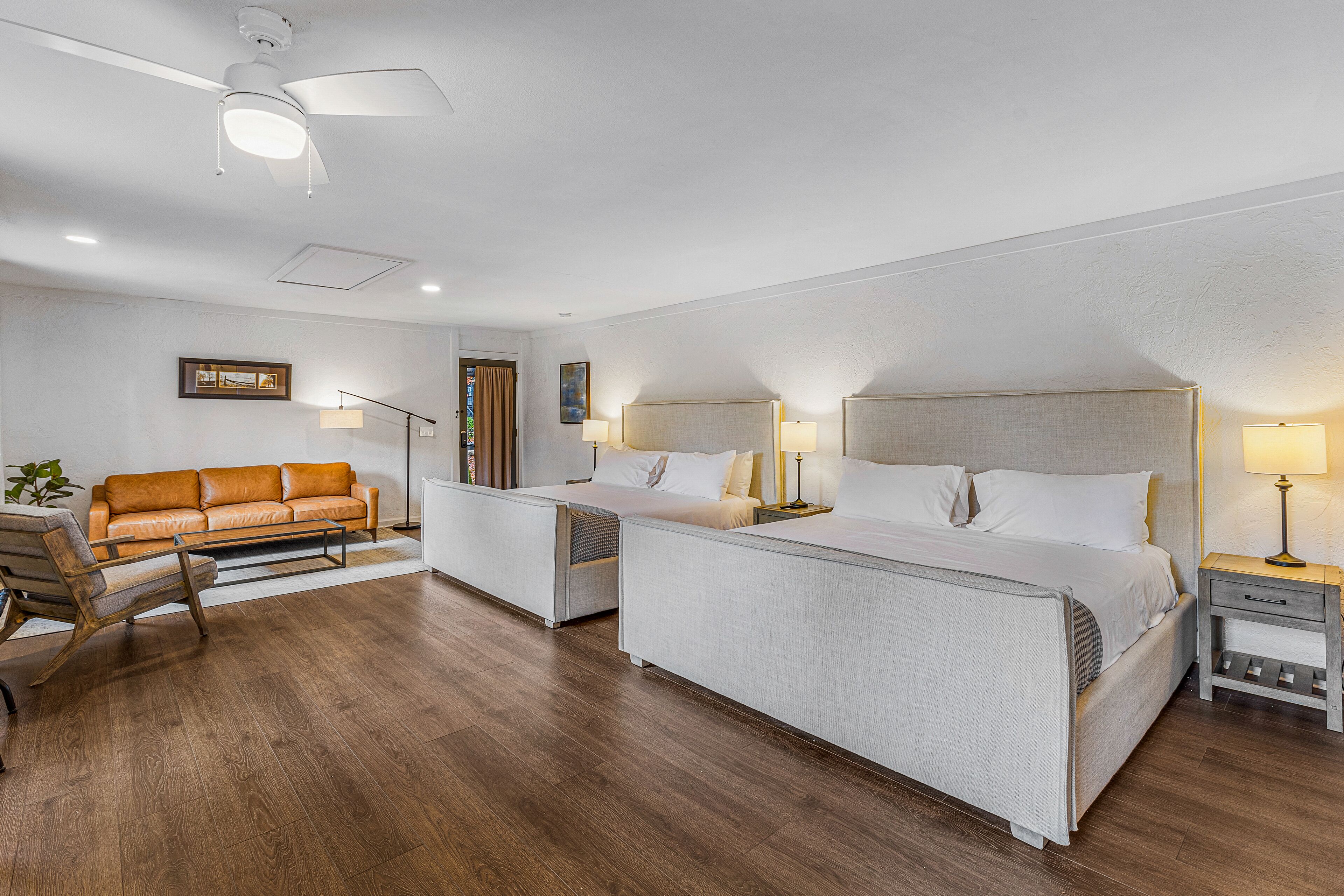 A hotel room with a large bed, a sofa, a desk, and a ceiling fan.