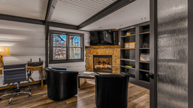 A modern living room with a stone fireplace, wooden flooring, and black leather furniture. - The Wells Hotel Cashiers (Cashiers)