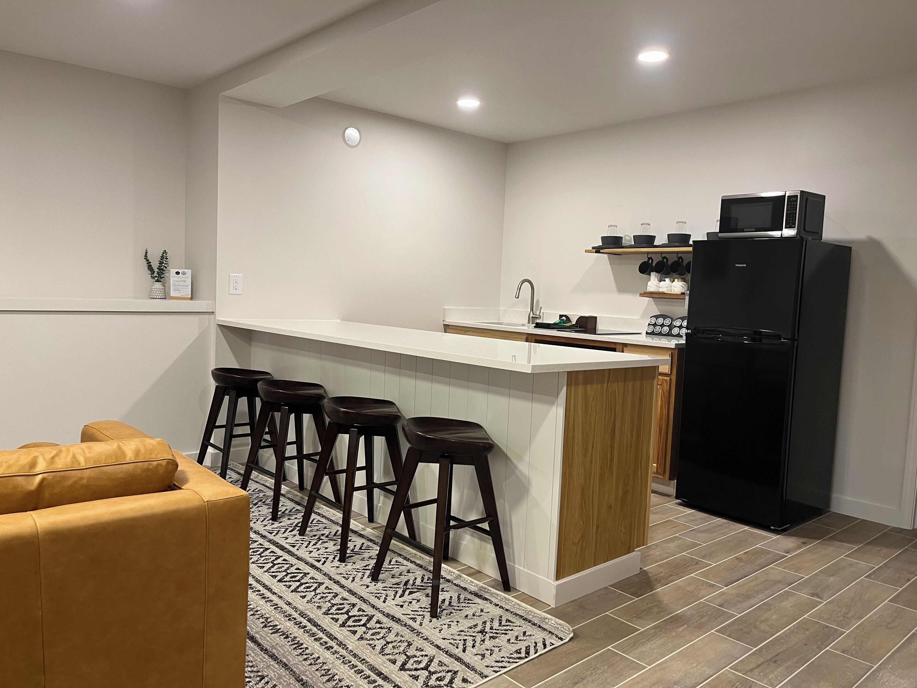A modern kitchen with a white countertop, black refrigerator, and wooden stools.