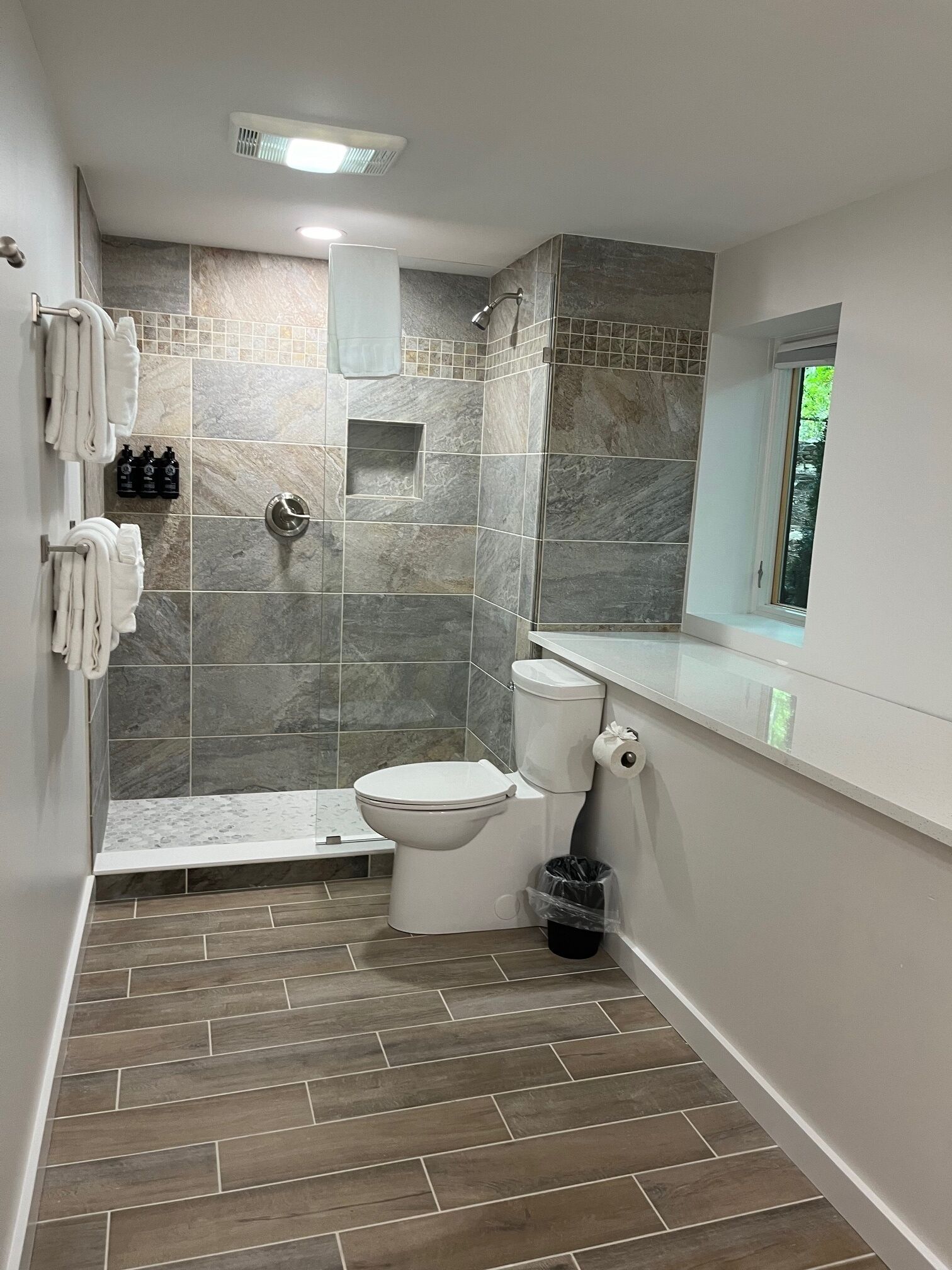 A bathroom with a shower, toilet, and a window.