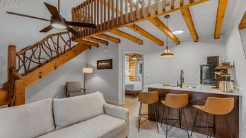 A modern interior with a wooden staircase, a sofa, and a kitchen area with bar stools.