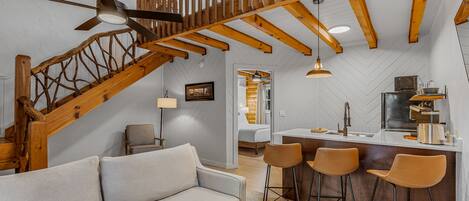 Um interior moderno com escada de madeira, sofá e área de cozinha com banquetas.