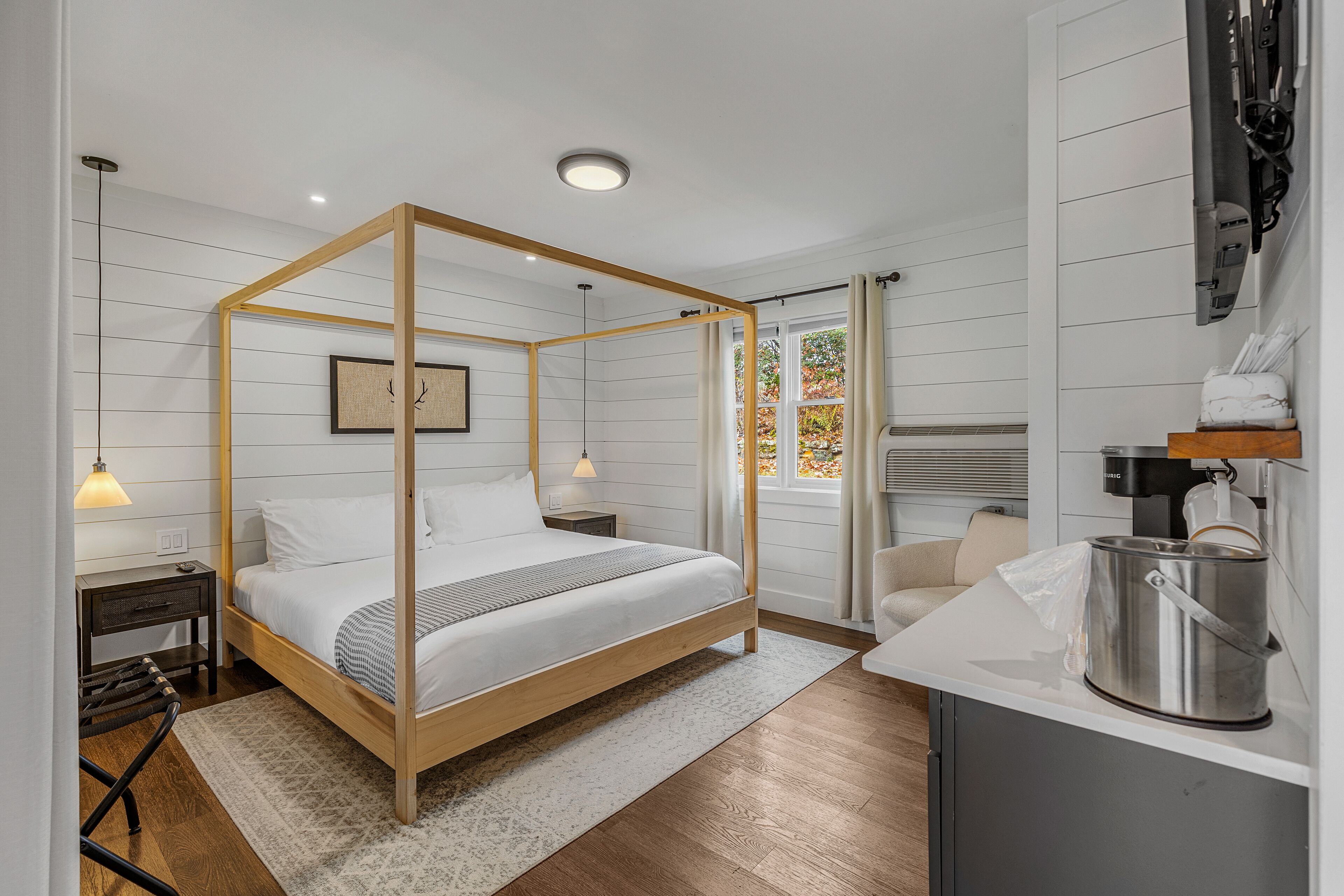 Un dormitorio moderno con cama con dosel, una mesita de noche, un pequeño escritorio y una zona de cocina con estufa.