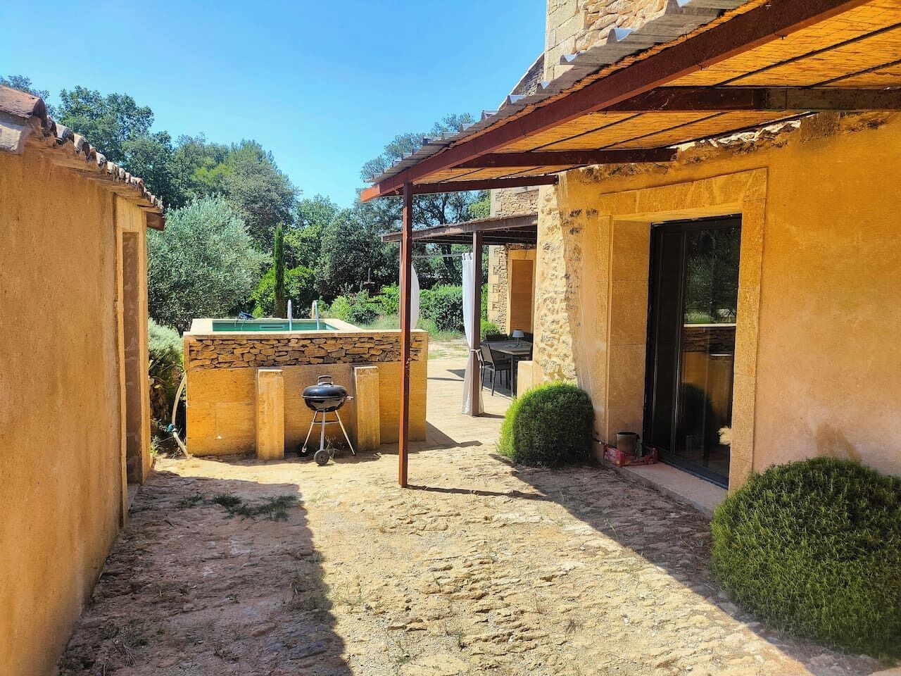 A covered outdoor area with a barbecue grill, a stone wall, and a patio with a table and chairs.