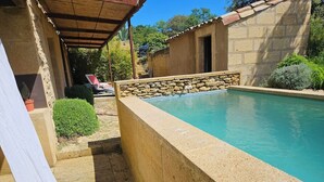 A pool with a stone wall, a covered area, and a stone building in the background.
