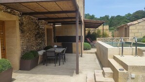 A covered outdoor patio with a table and chairs, a stone wall, and a pool area.