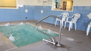 A small indoor pool with a metal ladder, white plastic chairs, and a blue tiled wall. - The Non-Smoking King Room (Vernal)