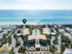 An aerial view of a coastal hotel with multiple buildings, a central swimming pool, and a beach in the background. - HP 34E On the Gulf @ High Pointe | Lagoon Pool | Tennis & Pickleball Courts (High Pointe Resort)