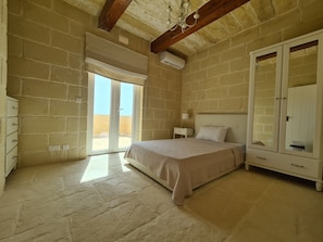 A bedroom with a bed, a nightstand, a dresser, and a wardrobe. There is a sliding glass door leading to an outdoor area. - Converted Detached Farmhouse/Villa with a 60sq mtr Pool, Deck Area and Garden. (Gharb)