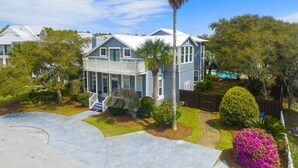 A two-story house with a balcony, a front porch, and a swimming pool in the background. - Spacious Retreat with Private Pool, Outdoor Oasis w/Firepit & Grill, and 8 Bikes (Seacrest Beach West)